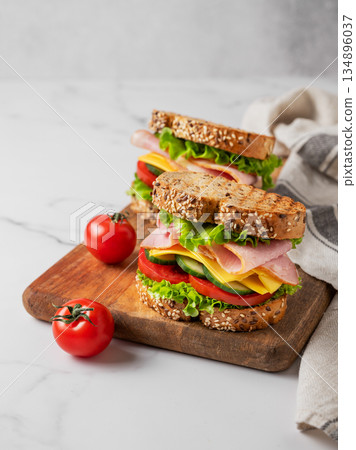 Two sandwiches with ham, cheese, lettuce, vegetables and seeded bread on a wooden board Two sandwiches with ham, cheese, lettuce, vegetables and seeded bread on a wooden board 134896037