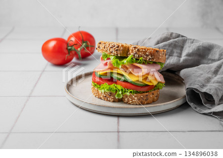 Sandwich with ham, cheese, lettuce and tomatoes on a plate on a gray tile background 134896038