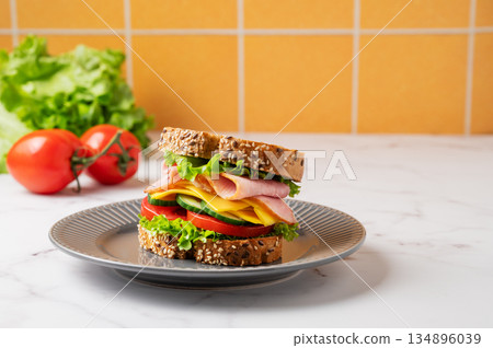 Sandwich with ham, cheese, lettuce and tomato on a plate on a marble table 134896039