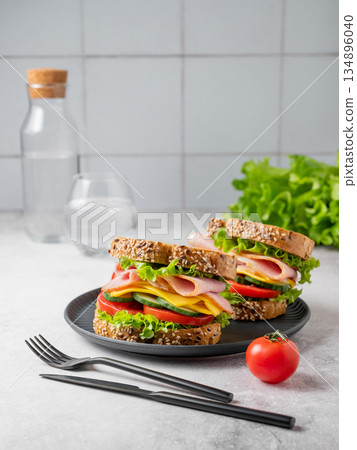 Two sandwiches with ham, cheese, lettuce and vegetable on a black plate on a concrete table Two sandwiches with ham, cheese, lettuce and vegetable on a black plate on a concrete table 134896040