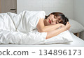 A Japanese woman sleeping warmly in bed under a duvet 134896173