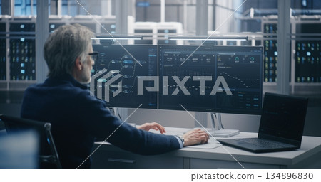 Senior Engineer Monitoring Data Flow on Dual Screens and Laptop 134896830
