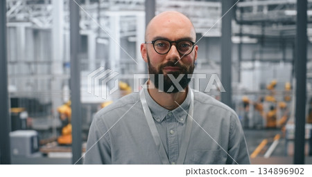 Dedicated Male Technical Specialist Poses Confidently in Front Automated Plant Containing Machinery Dedicated Male Technical Specialist Poses Confidently in Front Automated Plant Containing Machinery 134896902
