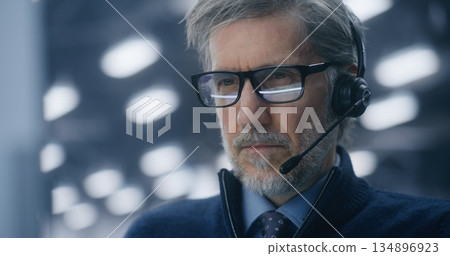 Professional IT Director With Glasses Intensely Communicating Via Headset From Modern Data Center Professional IT Director With Glasses Intensely Communicating Via Headset From Modern Data Center 134896923