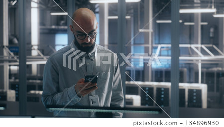 Bearded Male IT Engineer in Glasses Stands and Uses Smartphone to Check Critical Notifications 134896930
