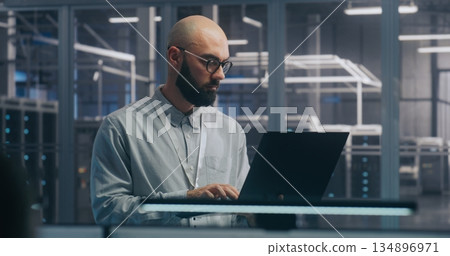 Focused IT Engineer Using Laptop in Server Hall 134896971
