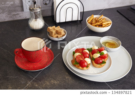 Bruschetta Caprese with mozzarella, cherry tomatoes, and basil on a plate. A cup of coffee and sugar nearby. Bruschetta Caprese with mozzarella, cherry tomatoes, and basil on a plate. A cup of coffee and sugar nearby. 134897821