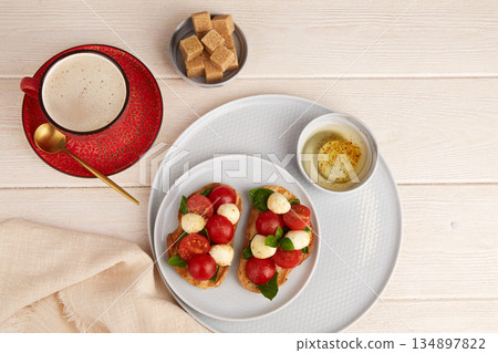 Bruschetta Caprese with mozzarella, cherry tomatoes, and basil on a plate. A cup of coffee and sugar nearby. 134897822