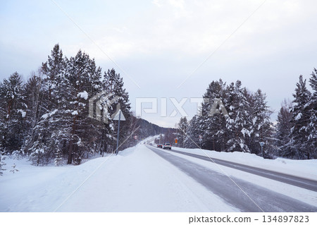 Cars drive along a road among a snowy winter forest 134897823