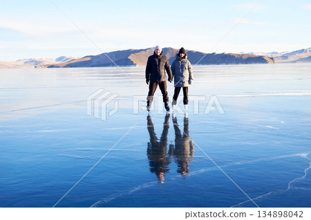 A couple is skating on the frozen Lake Baikal. Transparent ice. 134898042