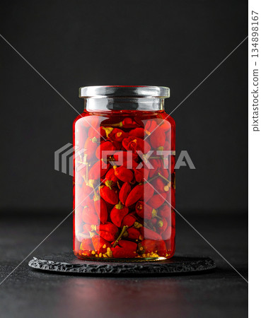 A simple glass jar is filled with small, bright red Akabanga chili oil drops for extra heat. 134898167