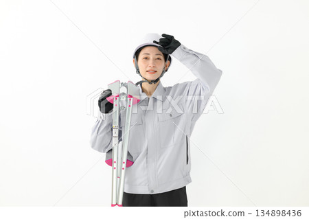 A woman in work clothes holding a stepladder 134898436