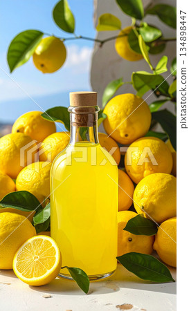 A bottle of bright yellow limoncello sits next to a pile of fresh lemons and leaves. 134898447