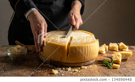 A person is shown breaking a large wheel of aged parmigiano reggiano cheese with a small knife. A person is shown breaking a large wheel of aged parmigiano reggiano cheese with a small knife. 134898448