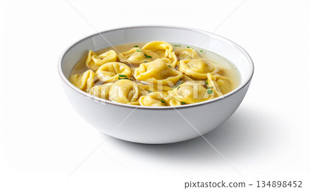A shallow bowl of clear broth contains several small, handmade tortellini pasta filled with meat. 134898452