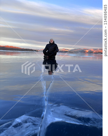 A man walks on the ice of Lake Baikal. A large crack on the transparent ice of the lake. A man walks on the ice of Lake Baikal. A large crack on the transparent ice of the lake. 134898485
