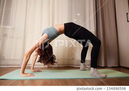 A fit woman practices yoga at home, doing the bridge pose. Home fitness A fit woman practices yoga at home, doing the bridge pose. Home fitness 134898506