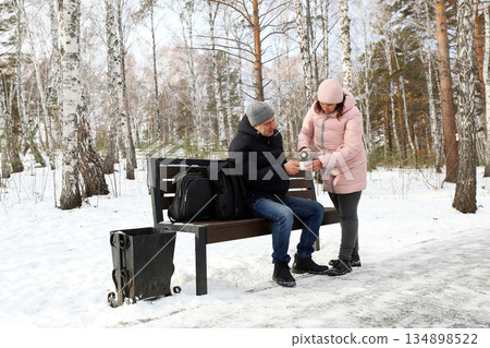 A man and a woman are relaxing on a bench in a snowy winter park 134898522