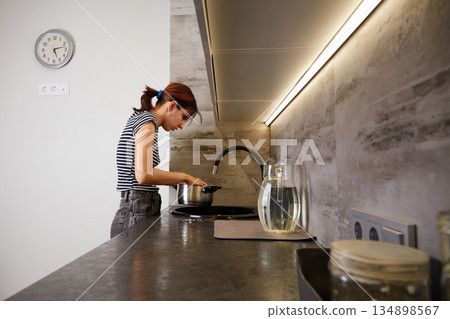 A young woman stands at the kitchen sink and washes dishes in a modern interior 134898567