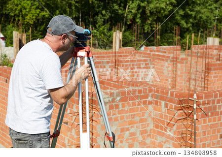 A construction worker checks the height level of the brickwork using a measuring tool on the construction site. A construction worker checks the height level of the brickwork using a measuring tool on the construction site. 134898958