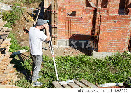 A construction worker checks the height level of the brickwork using a measuring tool on the construction site. A construction worker checks the height level of the brickwork using a measuring tool on the construction site. 134898962