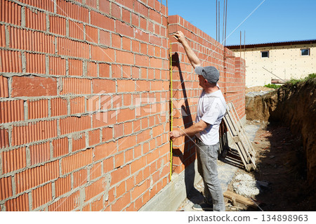 A construction worker is measuring a brick wall at a building site 134898963
