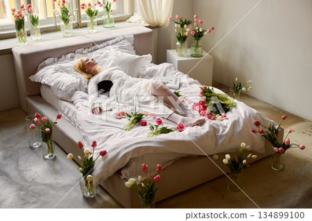 Woman relaxing among floral decor, Calm interior featuring woman with tulips and soft sunlight Woman relaxing among floral decor, Calm interior featuring woman with tulips and soft sunlight 134899100