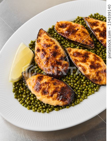 Delicious baked mussels presented over vibrant green peas on white plate 134899140