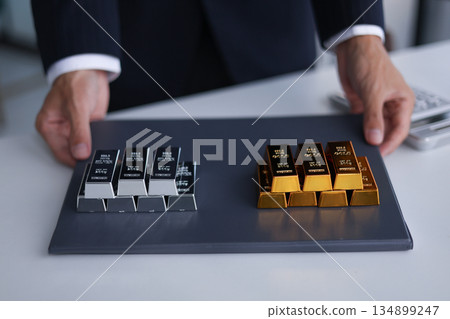 Gold and silver bars on the table. Businessman investing in precious metals to diversify portfolios hedge against inflation and currency depreciation. Gold and silver bars on the table. Businessman investing in precious metals to diversify portfolios hedge against inflation and currency depreciation. 134899247