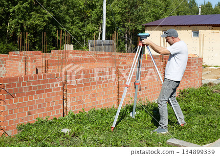 A construction worker checks the height level of the brickwork using a measuring tool on the construction site. A construction worker checks the height level of the brickwork using a measuring tool on the construction site. 134899339