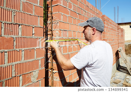 A construction worker is measuring a brick wall at a building site A construction worker is measuring a brick wall at a building site 134899341