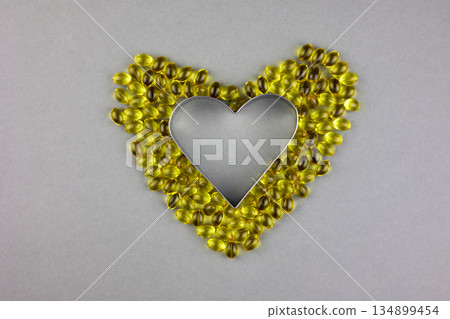 Gel yellow capsules with vitamin D3 on a gray background, laid out in the shape of a heart. Gel yellow capsules with vitamin D3 on a gray background, laid out in the shape of a heart. 134899454