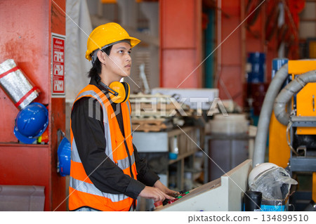 Young industrial worker operating control panel inside manufacturing facility. Focused on machine operation, the image represents factory training, automation, and responsibility. Young industrial worker operating control panel inside manufacturing facility. Focused on machine operation, the image represents factory training, automation, and responsibility. 134899510