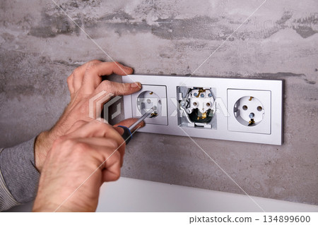 A man uses a screwdriver to install an electrical outlet on a porcelain tile wall A man uses a screwdriver to install an electrical outlet on a porcelain tile wall 134899600