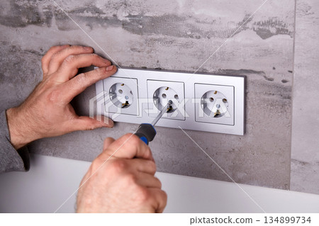 A man uses a screwdriver to install an electrical outlet on a porcelain tile wall 134899734