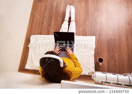 A girl with headphones is sitting on the floor and working on a laptop. . A girl with headphones is sitting on the floor and working on a laptop. . 134899750