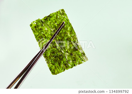 Chopsticks hold a piece of crispy dried seaweed. Nori, Japanese edible seaweed. 134899792