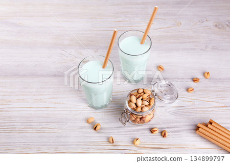 Pistachio milk in glasses with paper straws, nuts in jar on wooden background. 134899797