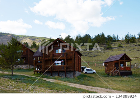 Rustic wooden cabins stand against a backdrop of hills and trees, creating a peaceful setting. Rustic wooden cabins stand against a backdrop of hills and trees, creating a peaceful setting. 134899924