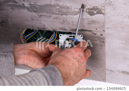 Electrician installing electrical outlets in a wall made of porcelain tiles. Electrician installing electrical outlets in a wall made of porcelain tiles. 134899925