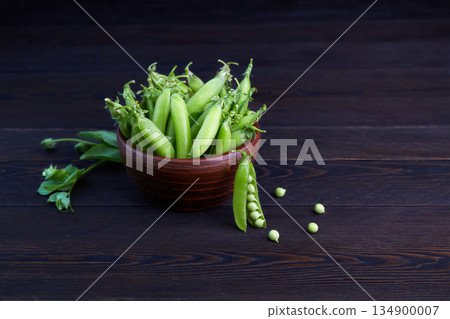 Pods of young green peas in bowl on a dark wooden background 134900007