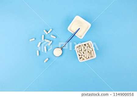 Collagen protein powder and capsules in jar, in spoon on blue background. Collagen protein powder and capsules in jar, in spoon on blue background. 134900058