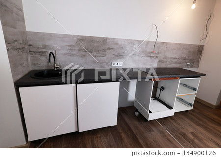 A newly installed kitchen countertop features a black sink and white cabinetry 134900126