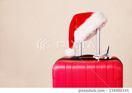 A red suitcase, a Santa Claus hat and a small airplane. 134900145