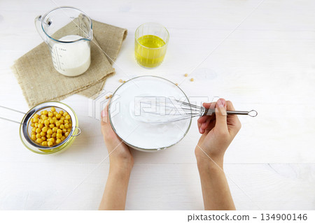 Aquafaba. A womans hand whips the liquid from the boiled chickpeas with a whisk. Aquafaba. A womans hand whips the liquid from the boiled chickpeas with a whisk. 134900146