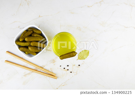 Pickled cucumbers in a bowl and pickle juice in glass on a light background. 134900225