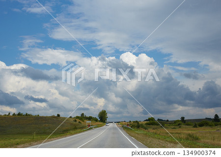 Cars drive along a paved road surrounded by vast meadows and hills. 134900374