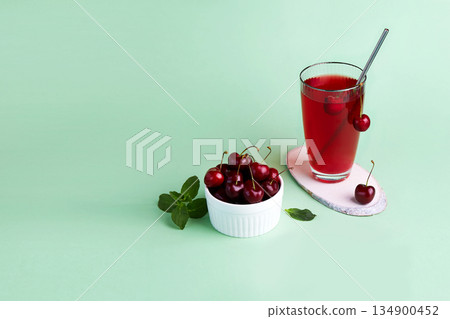 Cherry compote in a glass, berries in transparent bowl on a green background. Cherry compote in a glass, berries in transparent bowl on a green background. 134900452
