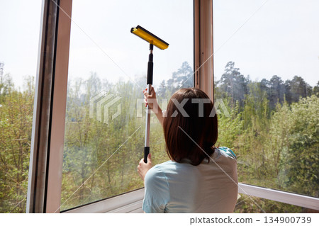 A young woman mops a large window, revealing a picturesque view of the street 134900739
