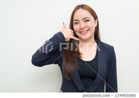 Portrait of a young Asian businesswoman against white background making call me phone hand gesture Portrait of a young Asian businesswoman against white background making call me phone hand gesture 134900866